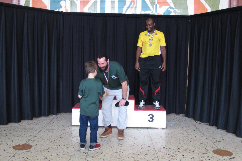 Matthieu reçoit la médaille d'or des mains d'Émile.  Ricardo médaille de bronze.